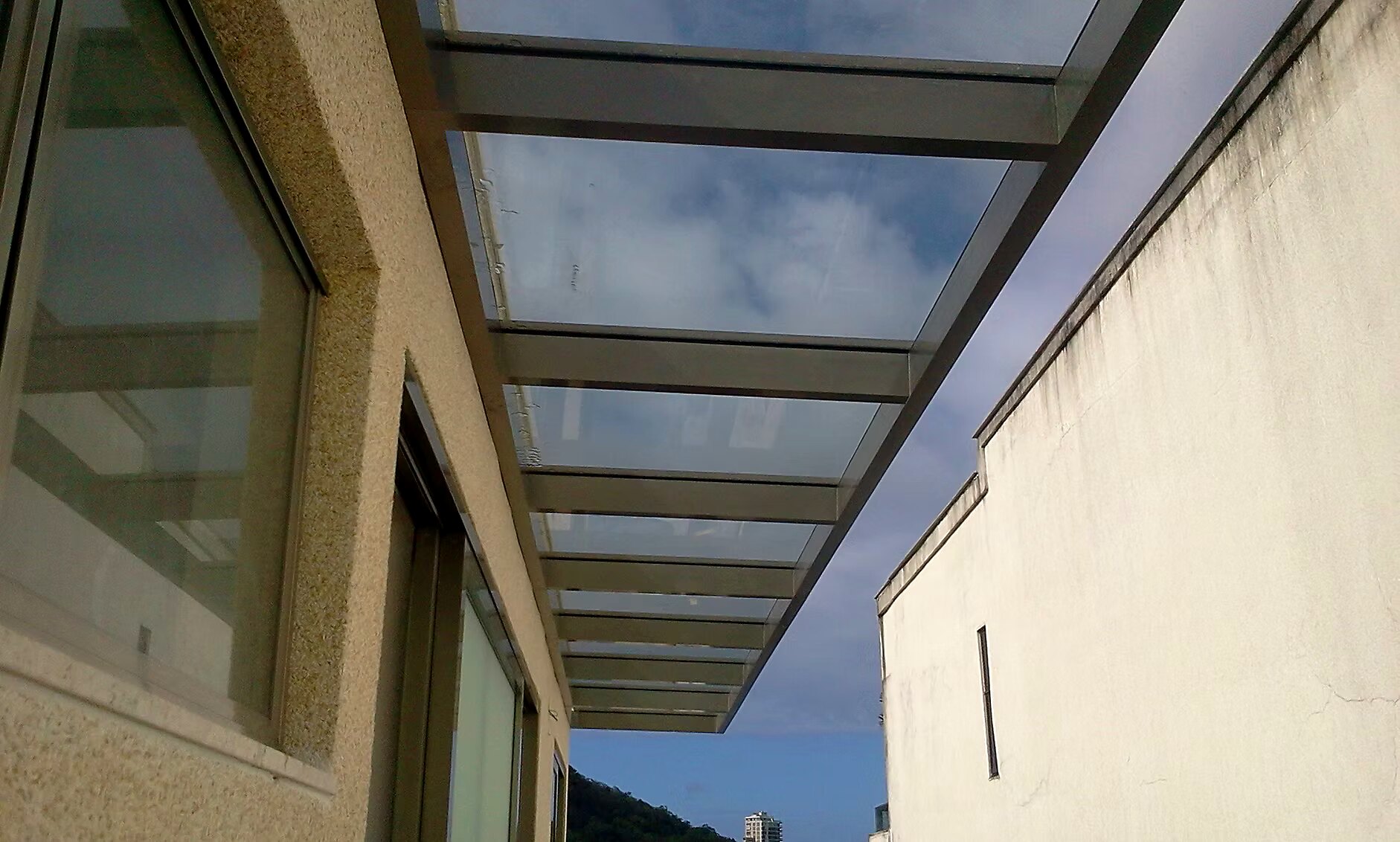 Cobertura em vidro com perfis de alumínio em corredor lateral entre dois edifícios, vista de baixo