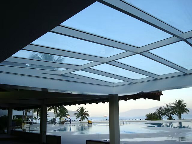 Cobertura em vidro com estrutura modulada vista de baixo, sobre área de piscina de resort