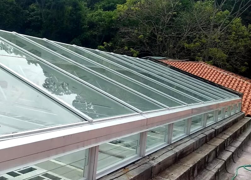 Cobertura em vidro modulado integrada a telhado colonial em meio à mata